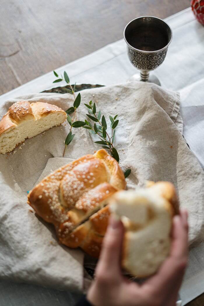 About Close-up of a Shabbat table setting featuring challah bread and a kiddush cup indoors.